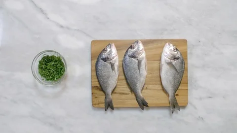 Putting fresh sea bream on table besides spices coriander Stock Footage 122235435
