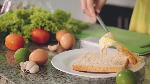 Putting fried egg on slice of bread, kitchen table with other ingredients Stock Footage 77904228