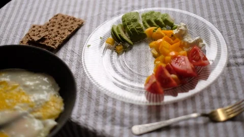 Putting fried eggs on the plate full of vegetables and cheese. Video stock 105358526