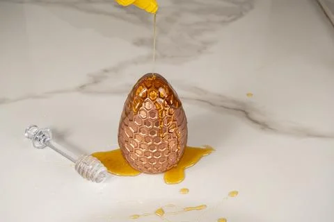 Putting honey on the chocolate Easter egg with honeycomb texture on the marbl Fotos de archivo