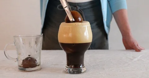 Putting ice in glass cup and pouring coffee with foam from shaker Stock Footage 106906509