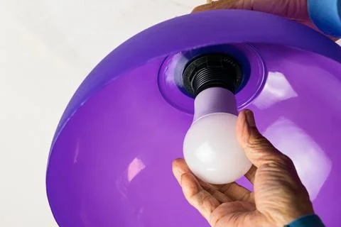 Putting led light bulb in the socket of purple pendant light. Foto stock
