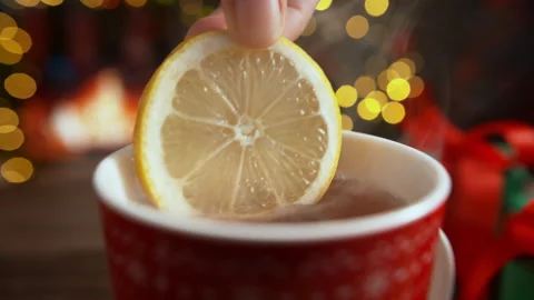 Putting a Lemon Slice in Hot Tea in Red Cup - Christmas Lights in the Background Stock Footage 208932111