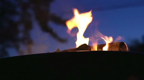 Putting log onto outdoor fire in the evening Stock Footage 23963143