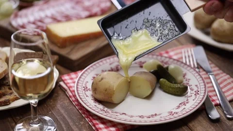 Putting melted raclette cheese on freshly boiled potatoes, swiss cuisine Stock Footage