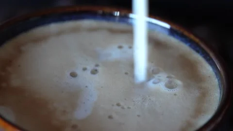 Putting milk in a cup of coffee on a table with coffee grounds on turn table, on Video stock 243295851