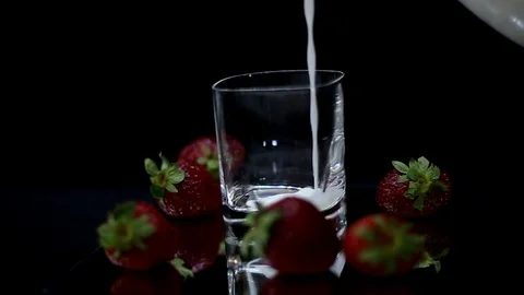 Putting milk inside the glass with fresh red strawberries on black background Video stock 109042867