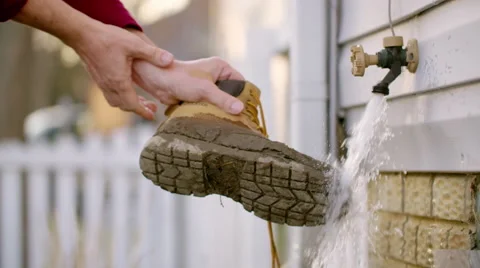Putting muddy boot under garden tap HD Stock Footage 48906946
