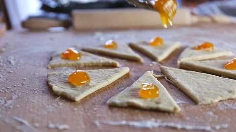 Putting orange marmalade on a raw triangles of dough on a board on the table Stock Footage 128699770