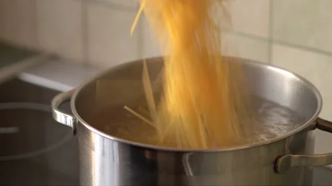 Putting pasta in pan in which water boiling stand on electric stove in kitchen Stock Footage 140337941