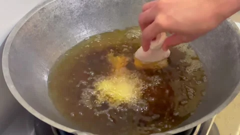 Putting raw chicken drumstick into hot frying oil in a large metal wok Stock Footage 327232298