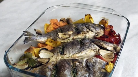 Putting roasted sea bream fish with with vegetable on table Stock Footage 122233286