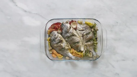 Putting roasted sea bream fish with vegetable on table Stock-Footage 122235506