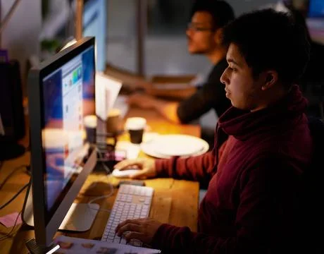 Putting in some overtime. a group of young coworkers working in a dimly-lit Foto stock