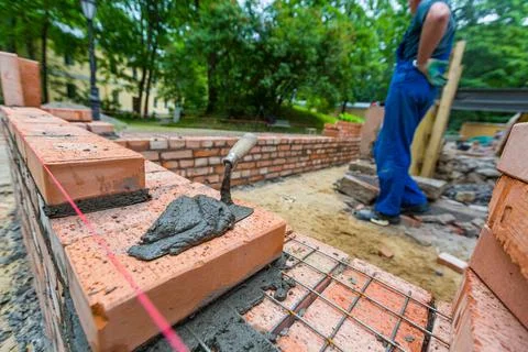 Putty knife with cement and bricklayer is near brickwork on exterior wall on Stock Photos