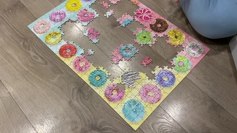 Puzzle on the floor assembled around the edges with an illustration of donuts Stock Footage 242344243