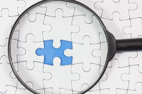 A puzzle with one piece missing and a magnifying glass. business and success Stock Photos