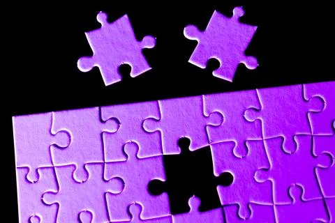 A puzzle with two pieces missing and a purple piece in the middle Stock Photos