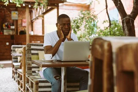 Puzzled and confused multicultural dark skin man using laptop, sit in cafe Stock Photos