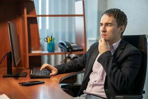 Puzzled businessman looking at a computer screen with his hand on his chin,.. Stock Photos