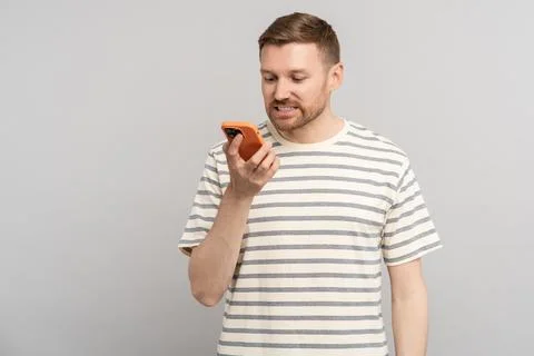 Puzzled man receiving sms reading frustrating message in smartphone on grey Stock-Fotos