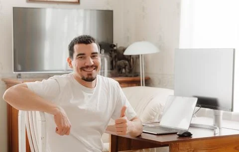 Puzzled man at a table with a computer with a hand near his face Stockfoto's