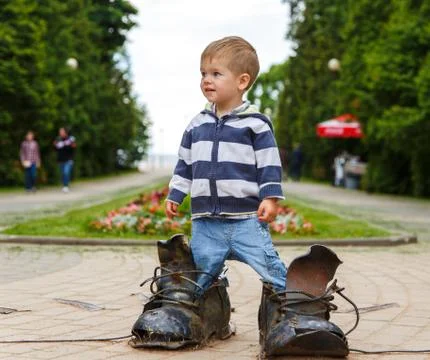 Puzzled two years old boy standing in giant boots Stock Photos