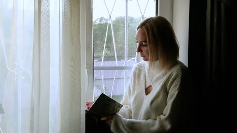 A puzzled Woman makes notes in her diary and looks out the window Stock Footage 114488259