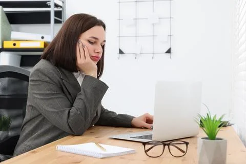 Puzzled young intern using laptop at table in modern office. First work day Stockfoto's