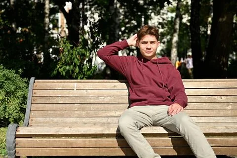 Puzzled young man on a bench looking at the camera and scratching the back .. Stock Photos