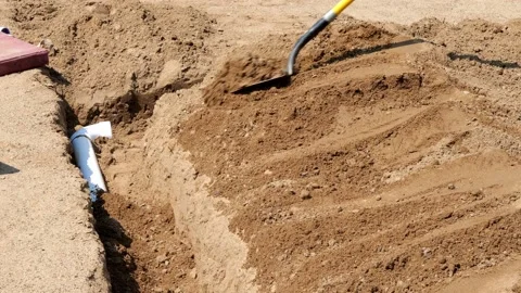 PVC pipe in a trench is being covered with dirt by a worker using a shovel. Stock Footage 158317464