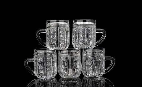 Pyramid of five empty crystal mugs on a black background with reflection. Stock Photos