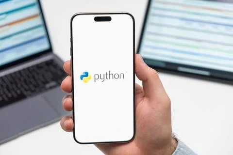 Python logo on the screen of smartphone in mans hand on the workplace background Stock Photos