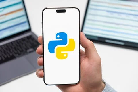 Python logo on the screen of smartphone in mans hand on the workplace background Stock Photos