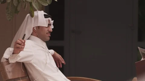 Qatari man sitting on bench and listening music. Stock Footage 90819964