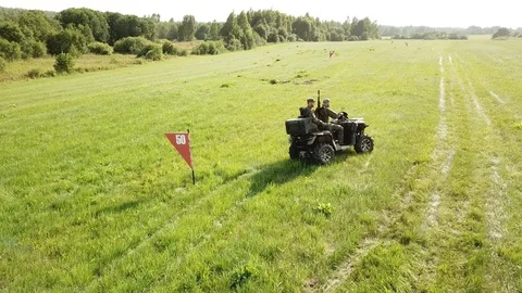 Quadcopter fly over the field following military men on a quad bike Stock Footage 93003142