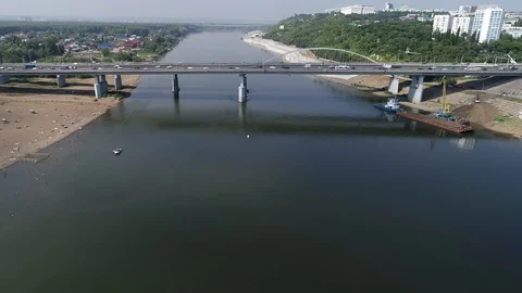 Quadcopter flying over the river and approaching bridge leading into the city. Stock Footage 127893372
