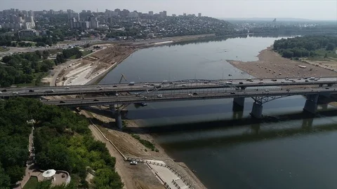 Quadcopter flying parallel to the bridge with two-way traffic over the river Stock Footage 127894747