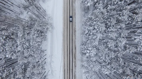 Quadcopter rises over the road in the forest on which the car moves. Winter snow Stock Footage 103231295