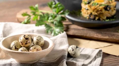 Quail eggs in a ceramic bowl on a rustic kitchen table Foto stock