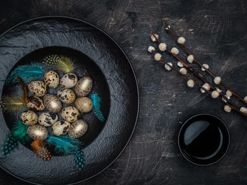 Quail eggs, golden colored eggs and colorful feathers in black bowl. Stock Photos