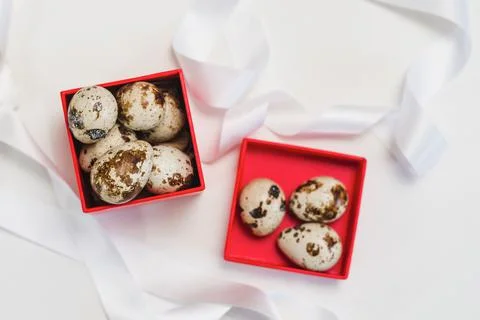 Quail eggs in a red box on a background of white ribbons Stock Photos