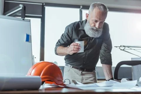 Qualified elderly engineer is drinking espresso in office 스톡 사진