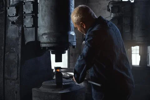 Qualified forge worker in overalls hitting molten metal Stock Photos