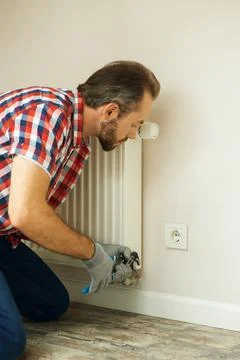 Quality help. Handyman using pipe wrench while repairing radiator battery in the Stock Photos