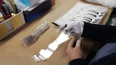 Quality inspector examining polished stainless steel fork before wrapping it in Stock Footage 340279404