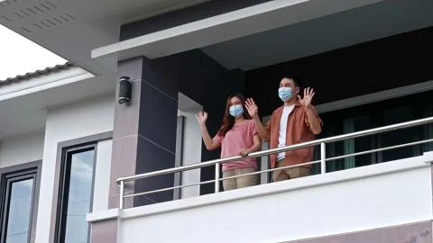 Quarantine couple wearing a face mask and greeting neighbors from balcony Stock Footage