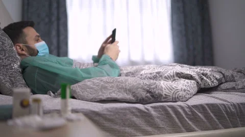 Quarantined man infected with virus lying in bed in protective clothes and Stock Footage 129493971