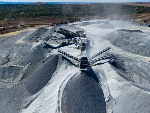 In a quarry, large machines work to process granite. Piles of gray stone mate Stock Photos