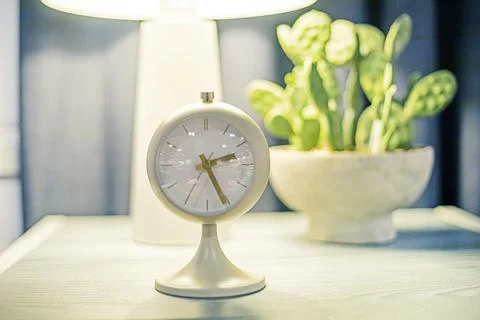 Quartz table clock on a nightstand with a flower and a light bulb. Time chang Stock Photos